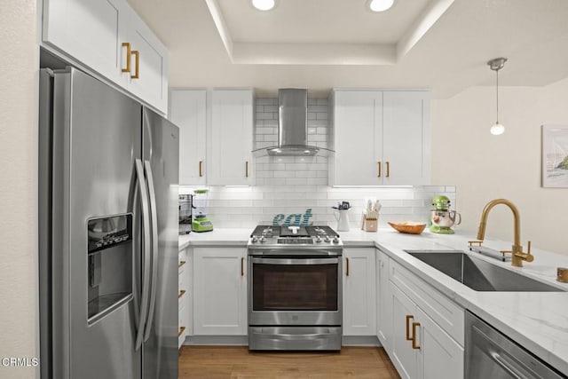 kitchen featuring a sink, appliances with stainless steel finishes, decorative backsplash, wall chimney exhaust hood, and a tray ceiling