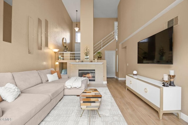 living room featuring visible vents, baseboards, light wood-style flooring, stairway, and a high ceiling