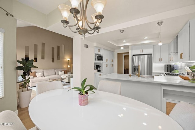 dining room with a tray ceiling, recessed lighting, visible vents, light wood-style flooring, and an inviting chandelier