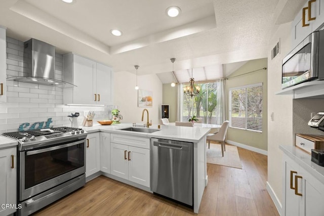 kitchen with wall chimney exhaust hood, a peninsula, stainless steel appliances, light countertops, and a sink