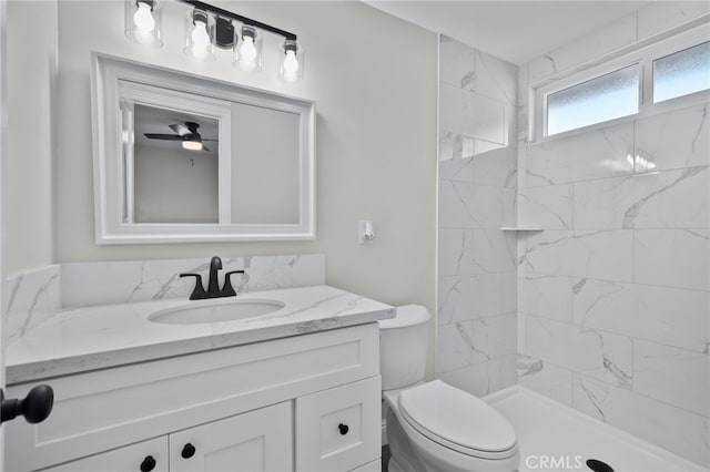 full bathroom with toilet, ceiling fan, a tile shower, and vanity