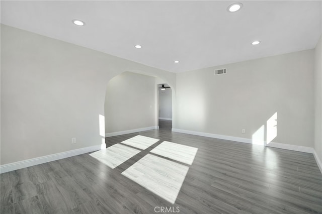 unfurnished room with baseboards, visible vents, arched walkways, wood finished floors, and recessed lighting