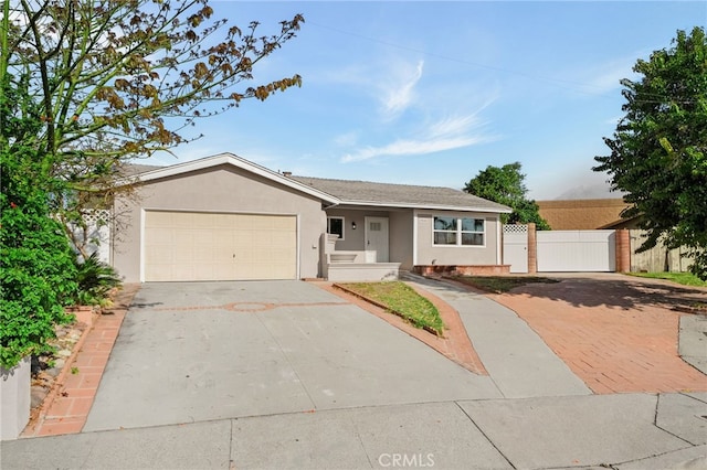 ranch-style home featuring concrete driveway, an attached garage, a gate, fence, and stucco siding