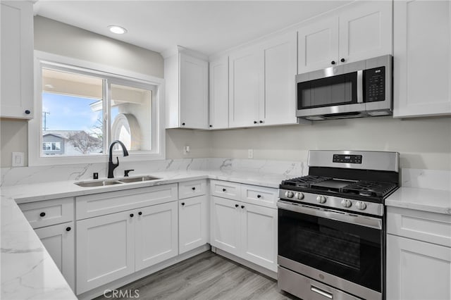 kitchen featuring a sink, white cabinetry, light wood-style floors, appliances with stainless steel finishes, and light stone countertops