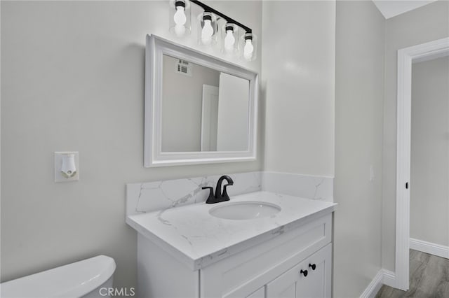 half bathroom with toilet, wood finished floors, vanity, visible vents, and baseboards