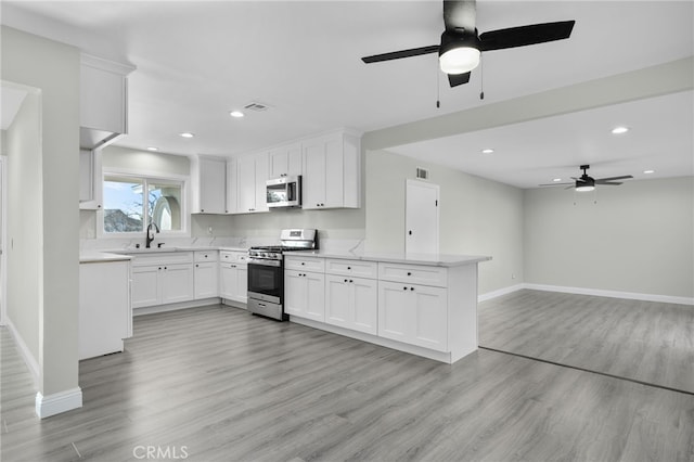 kitchen with stainless steel appliances, white cabinetry, and light wood-style floors