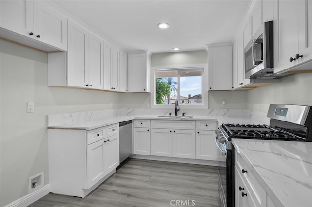 kitchen featuring white cabinets, light stone countertops, stainless steel appliances, and a sink