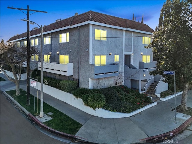 view of side of home with stairs, a tiled roof, and stucco siding