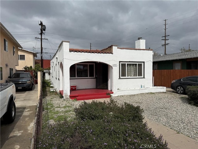 mediterranean / spanish-style home featuring a tile roof, fence, a chimney, and stucco siding