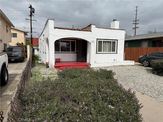 mediterranean / spanish home with a tiled roof, a chimney, fence, and stucco siding