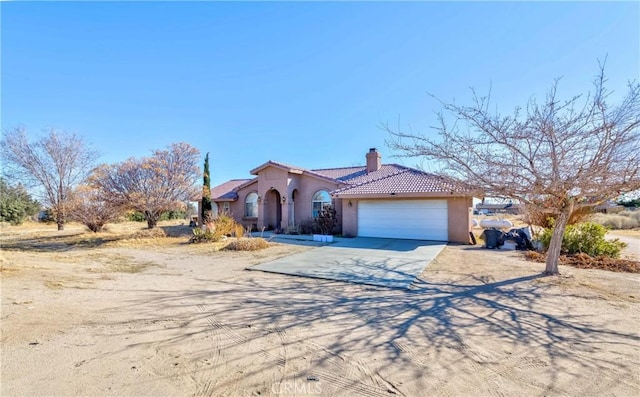 mediterranean / spanish-style house with a tile roof, a chimney, stucco siding, a garage, and driveway