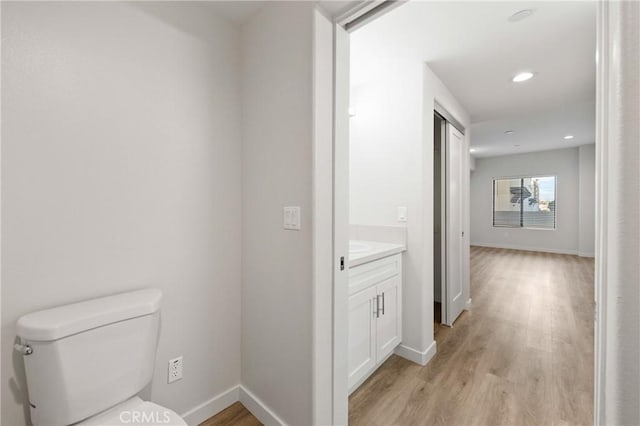 bathroom with toilet, vanity, baseboards, and wood finished floors