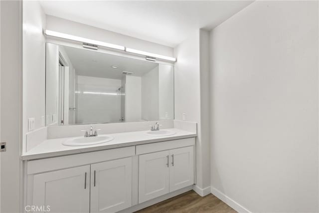 bathroom featuring double vanity, a shower, a sink, and wood finished floors