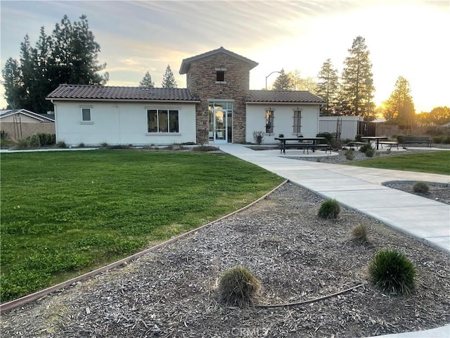 rear view of house featuring stucco siding, a lawn, fence, stone siding, and a tiled roof