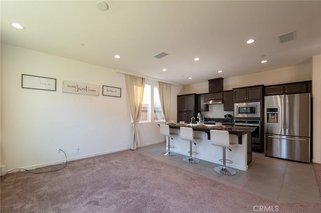 kitchen featuring a breakfast bar area, a kitchen island with sink, recessed lighting, stainless steel appliances, and dark brown cabinets