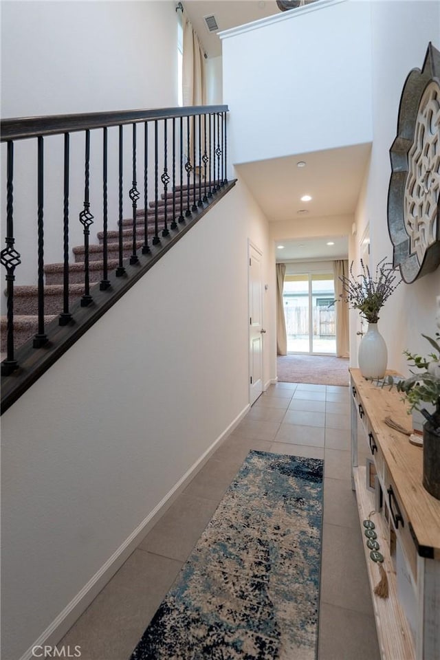 hallway with tile patterned flooring, visible vents, a towering ceiling, and baseboards