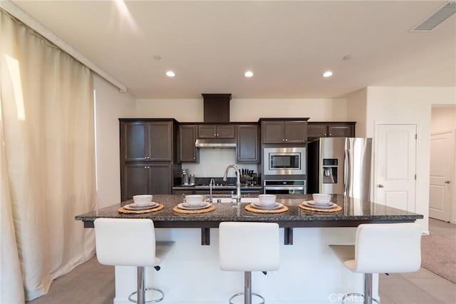 kitchen featuring dark brown cabinetry, visible vents, appliances with stainless steel finishes, a kitchen breakfast bar, and a sink