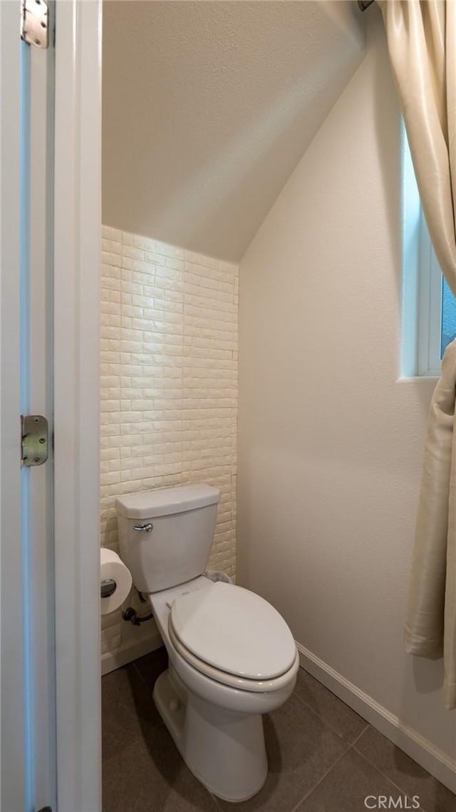 bathroom with baseboards, toilet, tile patterned floors, vaulted ceiling, and a textured ceiling