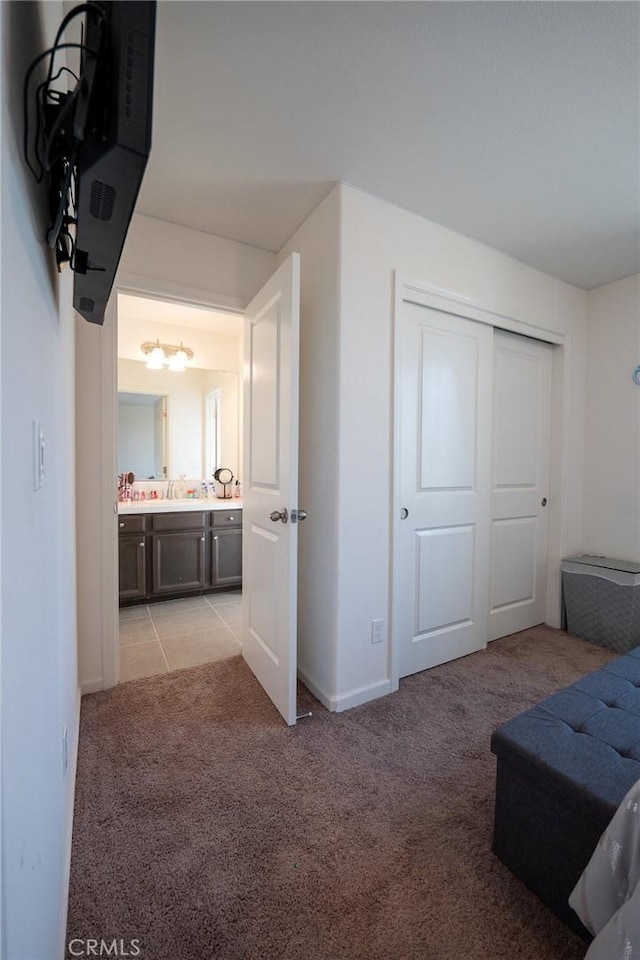 bedroom with a closet, ensuite bathroom, light carpet, a sink, and baseboards