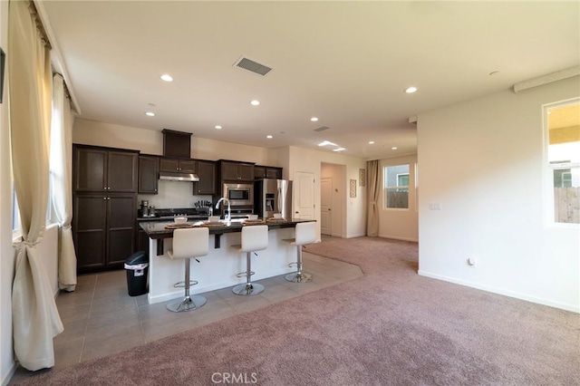 kitchen with visible vents, light colored carpet, appliances with stainless steel finishes, under cabinet range hood, and a kitchen bar