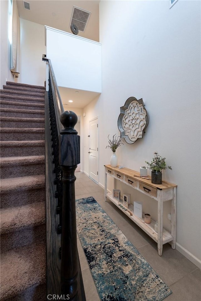 stairs with a high ceiling, tile patterned flooring, visible vents, and baseboards