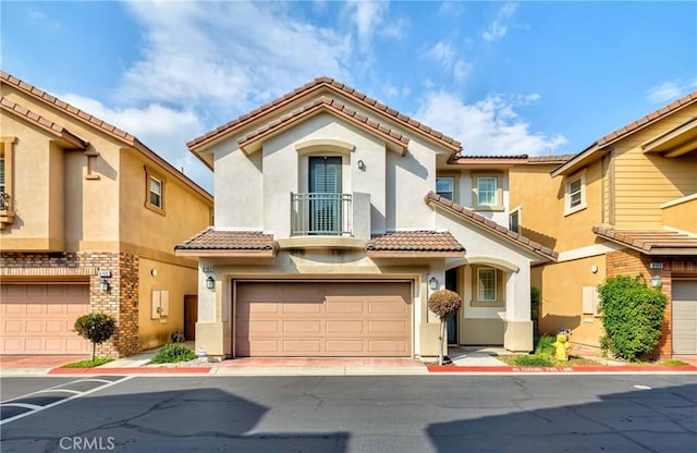 mediterranean / spanish house featuring a tile roof, an attached garage, and stucco siding