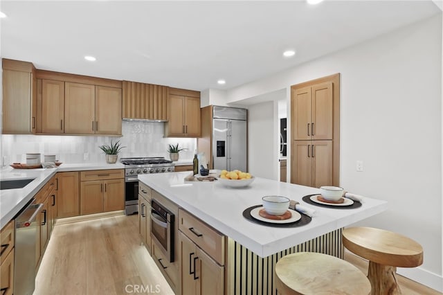 kitchen with a center island, high end appliances, light countertops, decorative backsplash, and light wood-style floors