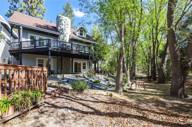 back of house featuring stone siding, a chimney, and a wooden deck