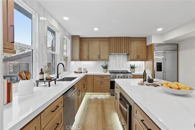 kitchen featuring a sink, light countertops, light wood-type flooring, decorative backsplash, and high end appliances