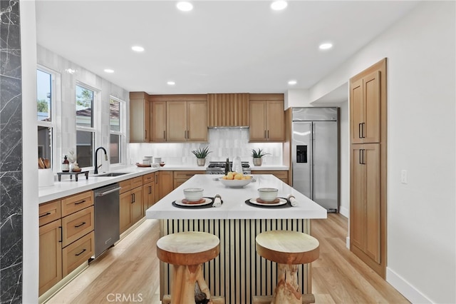 kitchen featuring stainless steel appliances, a sink, a kitchen breakfast bar, light wood-style floors, and light countertops