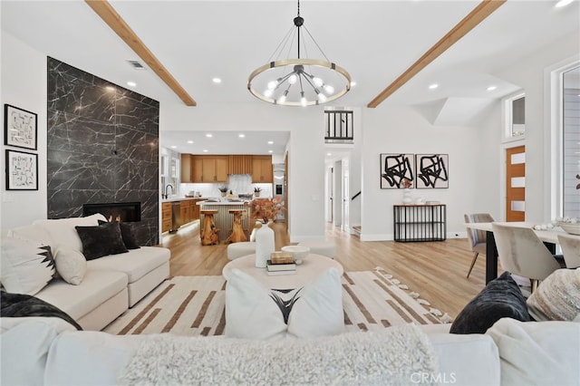 living area with a high end fireplace, beam ceiling, light wood-style flooring, and recessed lighting