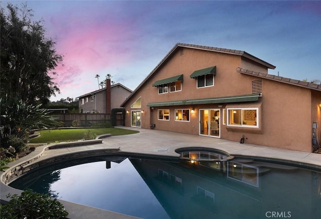 back of property at dusk featuring a yard, stucco siding, a patio, and fence