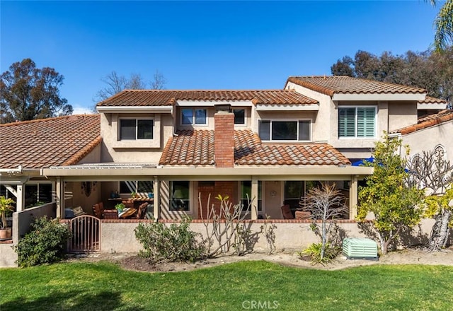 rear view of house with a yard, a tile roof, and stucco siding