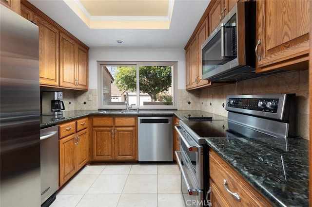 kitchen featuring stainless steel appliances, a tray ceiling, brown cabinetry, and a sink