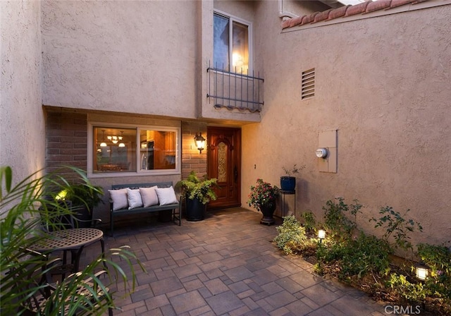 view of exterior entry with a patio area, a tile roof, a balcony, and stucco siding