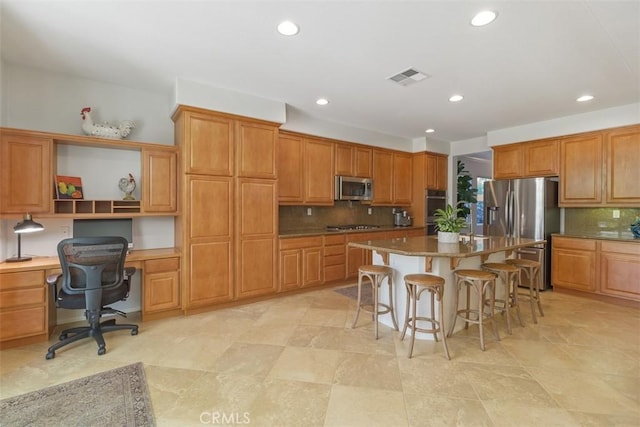 kitchen featuring visible vents, a breakfast bar area, appliances with stainless steel finishes, built in desk, and backsplash