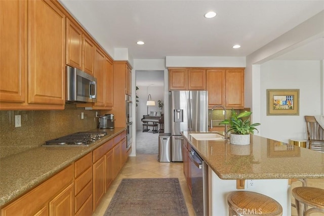 kitchen featuring stone countertops, stainless steel appliances, a sink, a kitchen breakfast bar, and decorative backsplash