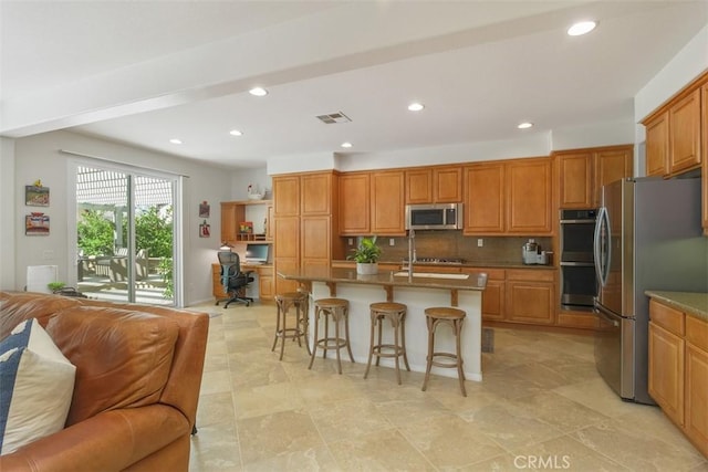 kitchen with stainless steel appliances, a breakfast bar, visible vents, open floor plan, and backsplash