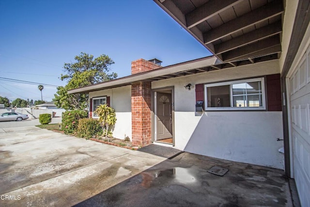 entrance to property with brick siding, a chimney, and stucco siding