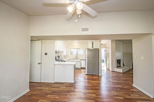 kitchen with white cabinets, dark wood finished floors, stainless steel appliances, light countertops, and a fireplace