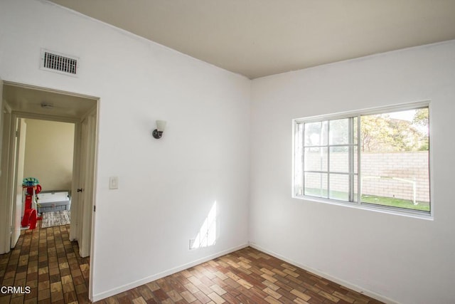 empty room featuring brick floor, visible vents, and baseboards