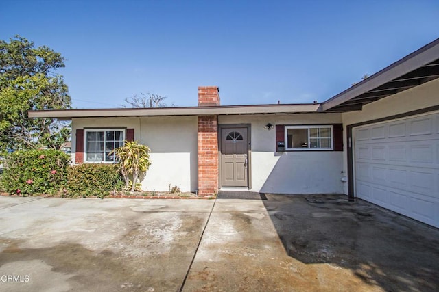 ranch-style house with a garage, driveway, a chimney, and stucco siding