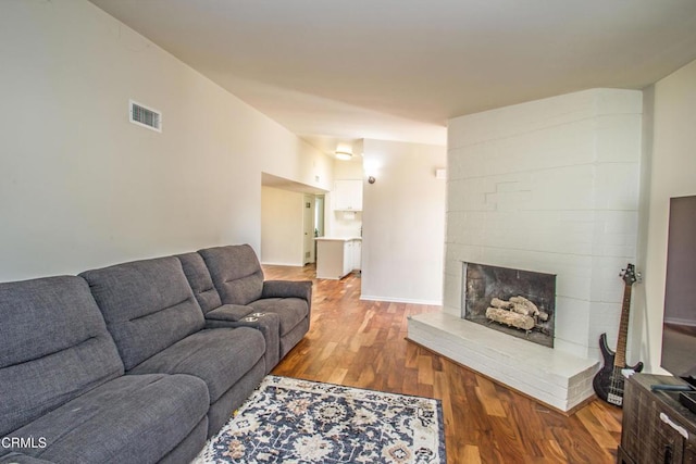 living room featuring baseboards, a fireplace, visible vents, and wood finished floors