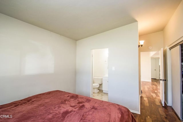 bedroom with lofted ceiling, wood finished floors, and ensuite bathroom