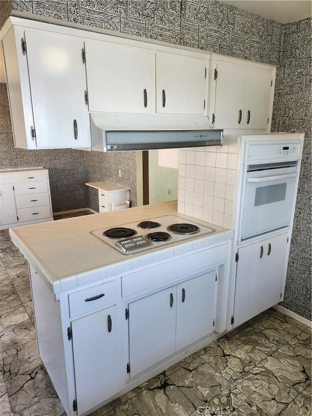 kitchen with white appliances, exhaust hood, white cabinetry, and decorative backsplash