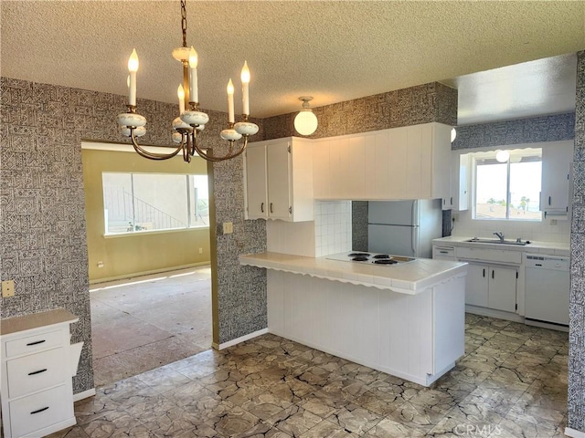 kitchen featuring backsplash, white cabinetry, a sink, white appliances, and a peninsula