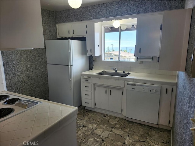 kitchen with white appliances, a sink, tile counters, and white cabinetry