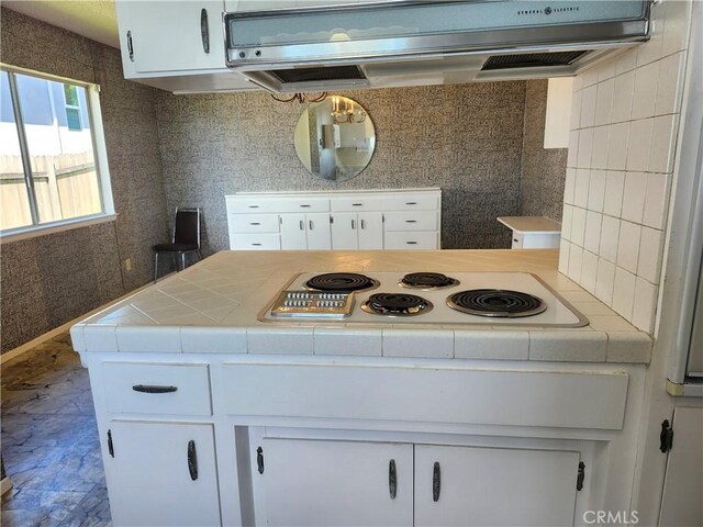 kitchen featuring white electric stovetop, white cabinetry, tile countertops, and wall chimney exhaust hood