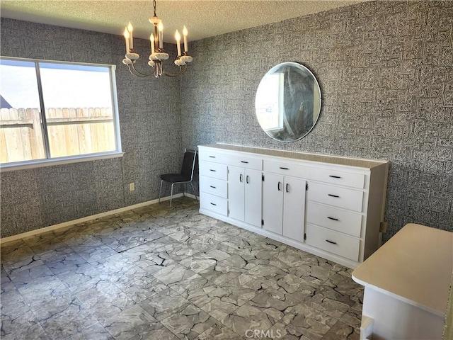 unfurnished dining area with a textured ceiling, a notable chandelier, and baseboards