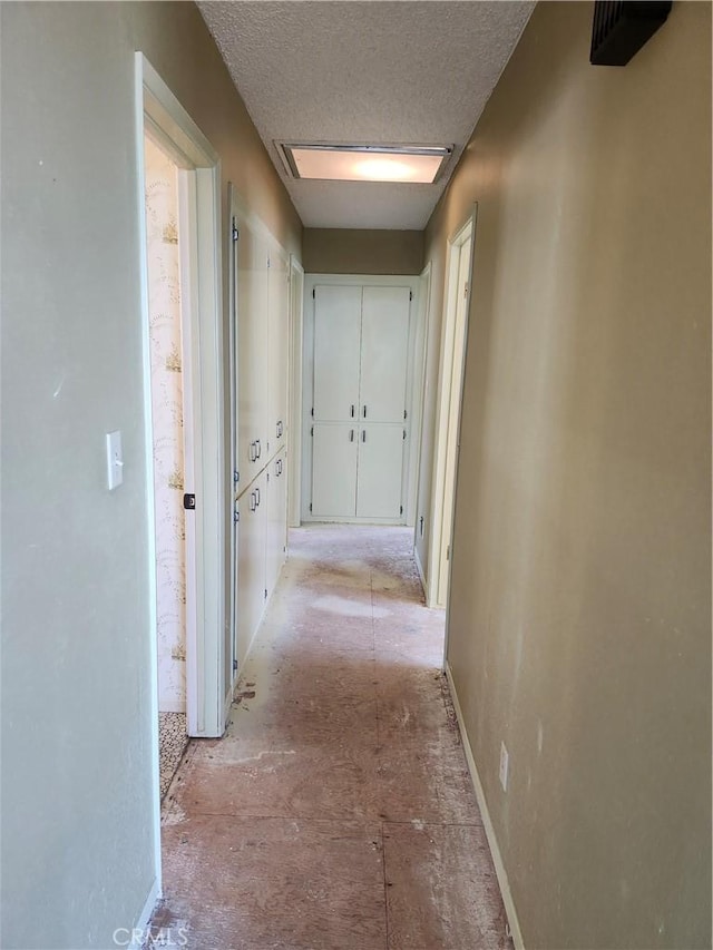 hall with a textured ceiling and baseboards